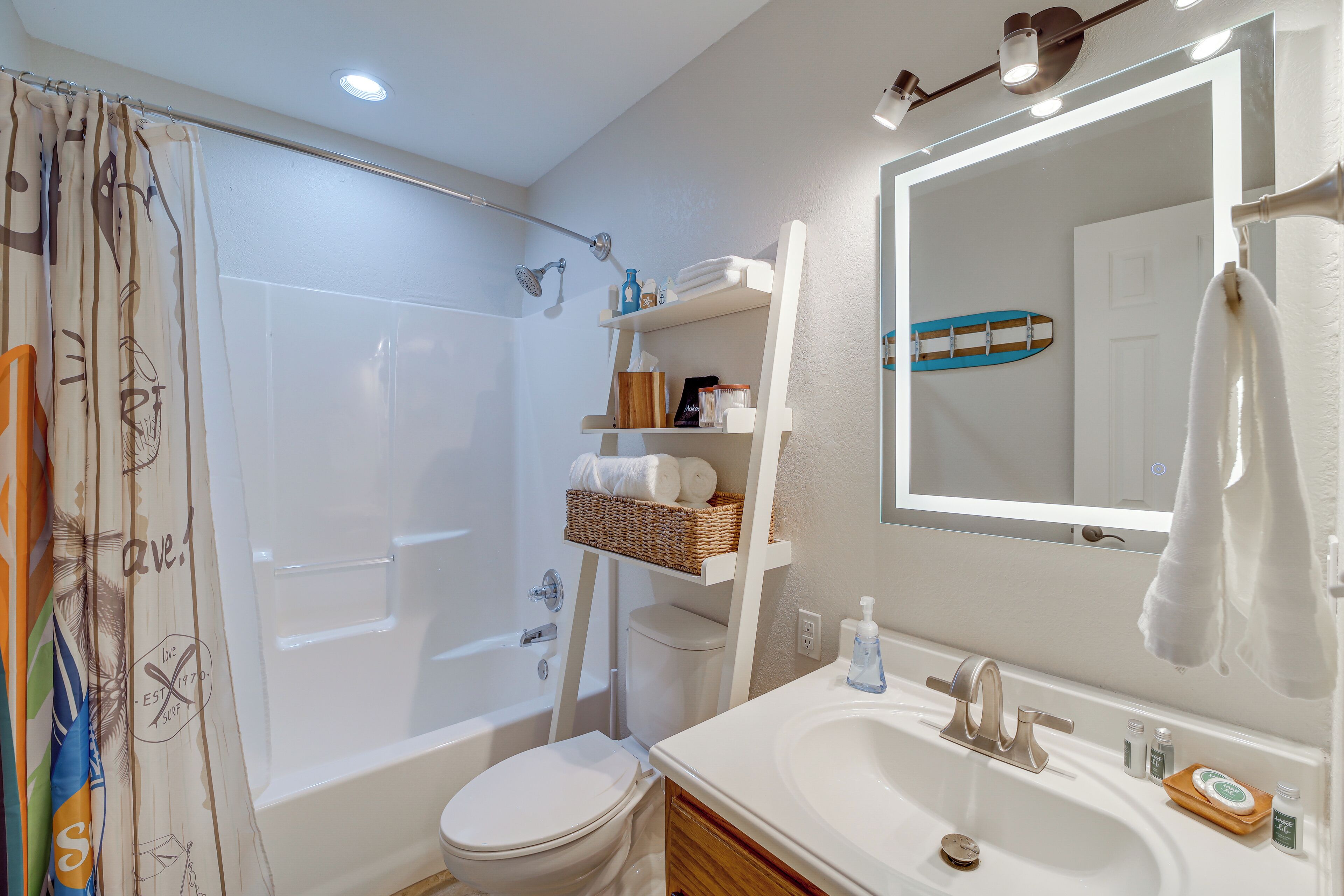 Une salle de bain avec une baignoire, des toilettes et un lavabo. Il y a un miroir au-dessus du lavabo et un rideau de douche à motifs.