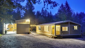 Une maison à deux étages, dotée d’un porche à l’avant et d’un garage, entourée d’arbres.