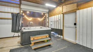 Un bain à remous dans une pièce dotée d’un plafond en bois, d’une fenêtre décorée de guirlandes lumineuses et d’une porte.
