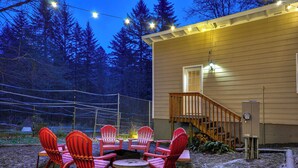 Une maison en bois dotée d’un patio couvert, agrémenté de chaises Adirondack rouges et d’une petite table.