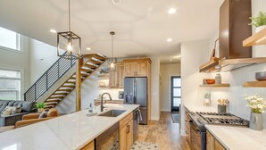 Une cuisine moderne dotée d’un îlot central, de meubles en bois, d’appareils électroménagers en acier inoxydable et d’un escalier menant à un autre niveau.