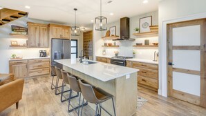 Une cuisine moderne avec des meubles en bois, un grand îlot central doté de tabourets, des appareils en acier inoxydable et un éclairage suspendu.