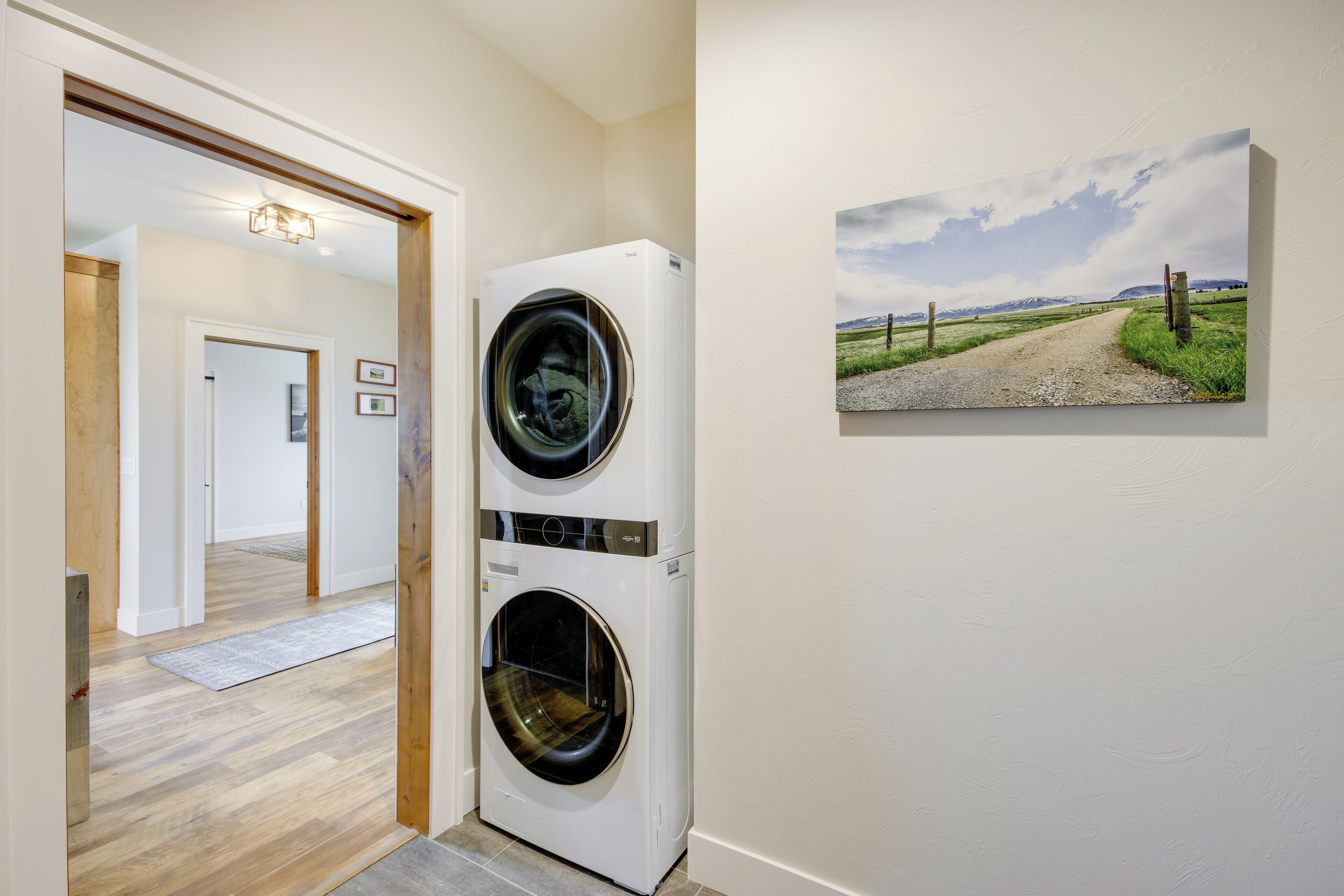 A laundry room with two stacked front-loading washing machines, a wooden floor, and a framed landscape painting on the wall.