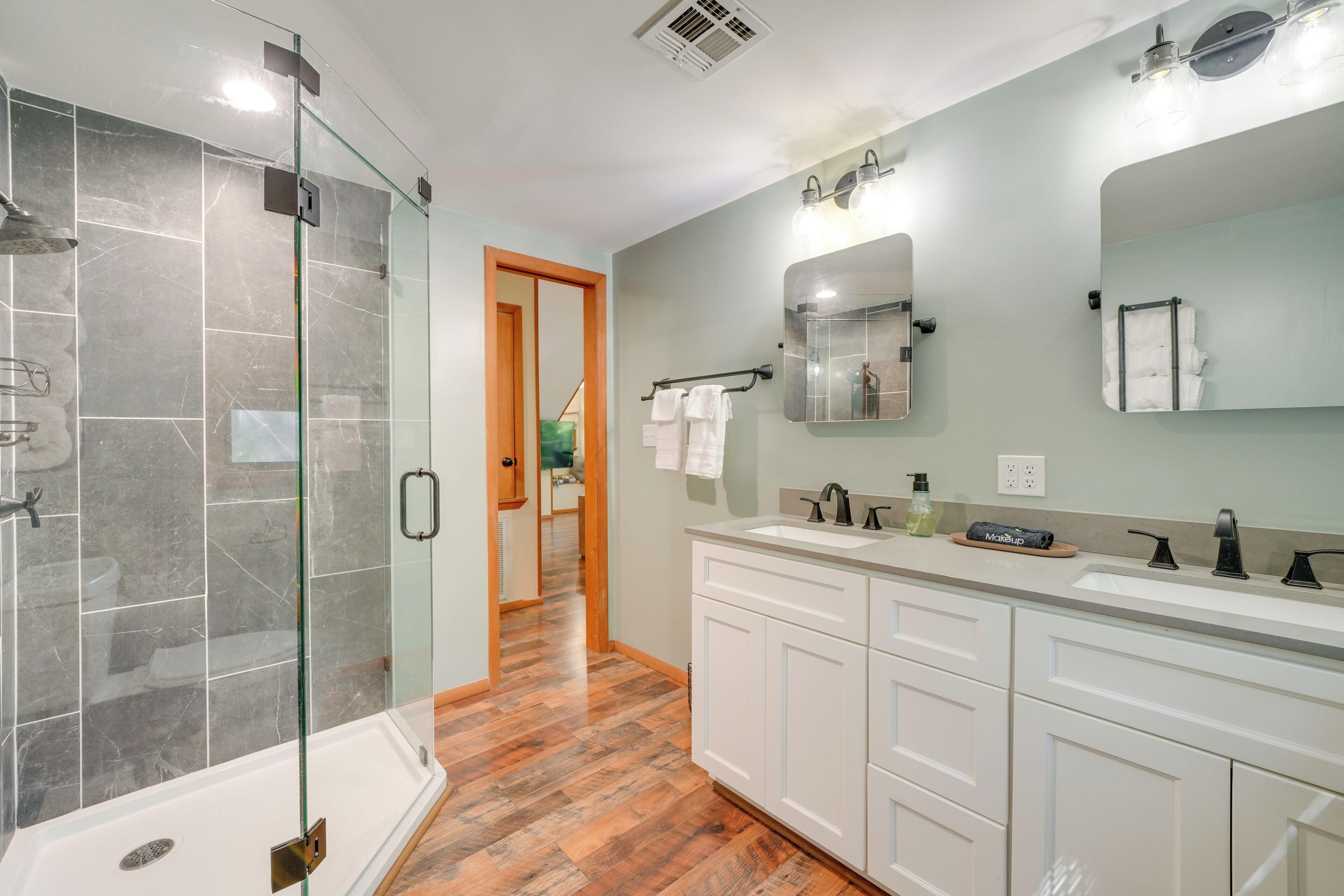 A modern bathroom with a glass-enclosed shower, white cabinetry, and a large mirror.