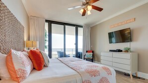 A bedroom with a bed, a ceiling fan, a TV, and a view of the outdoors. - Dauphin Island Condo in Holiday Isle With Balcony! (Dauphin Island)