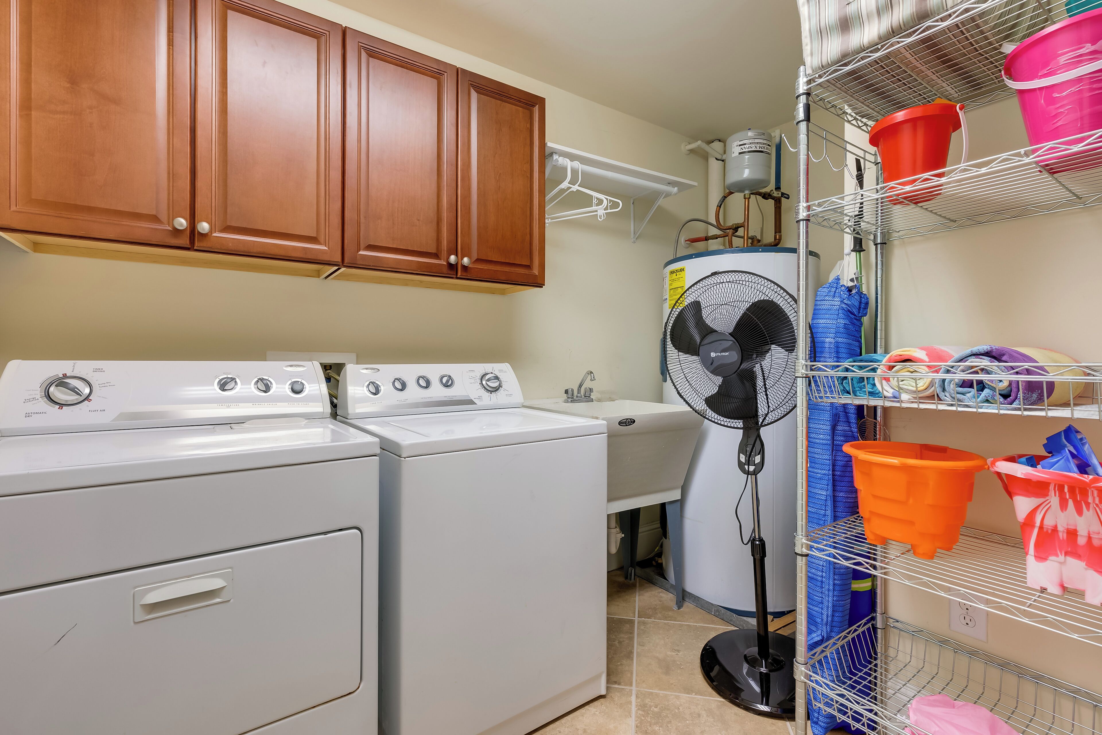 A laundry area with a washer and dryer, a sink, a fan, and shelves with various items.