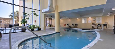 An indoor swimming pool with a clear view of the outside, a poolside seating area, and a clock on the wall.