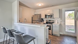 A modern kitchen with white cabinets, stainless steel appliances, and a bar area with stools. - Greer Getaway w/ Smart TV ~ 1 Mi to Dtwn! (Greer)