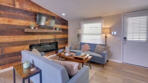 Una sala de estar con chimenea, un sofá, una mesa de centro y un televisor montado en una pared de madera.