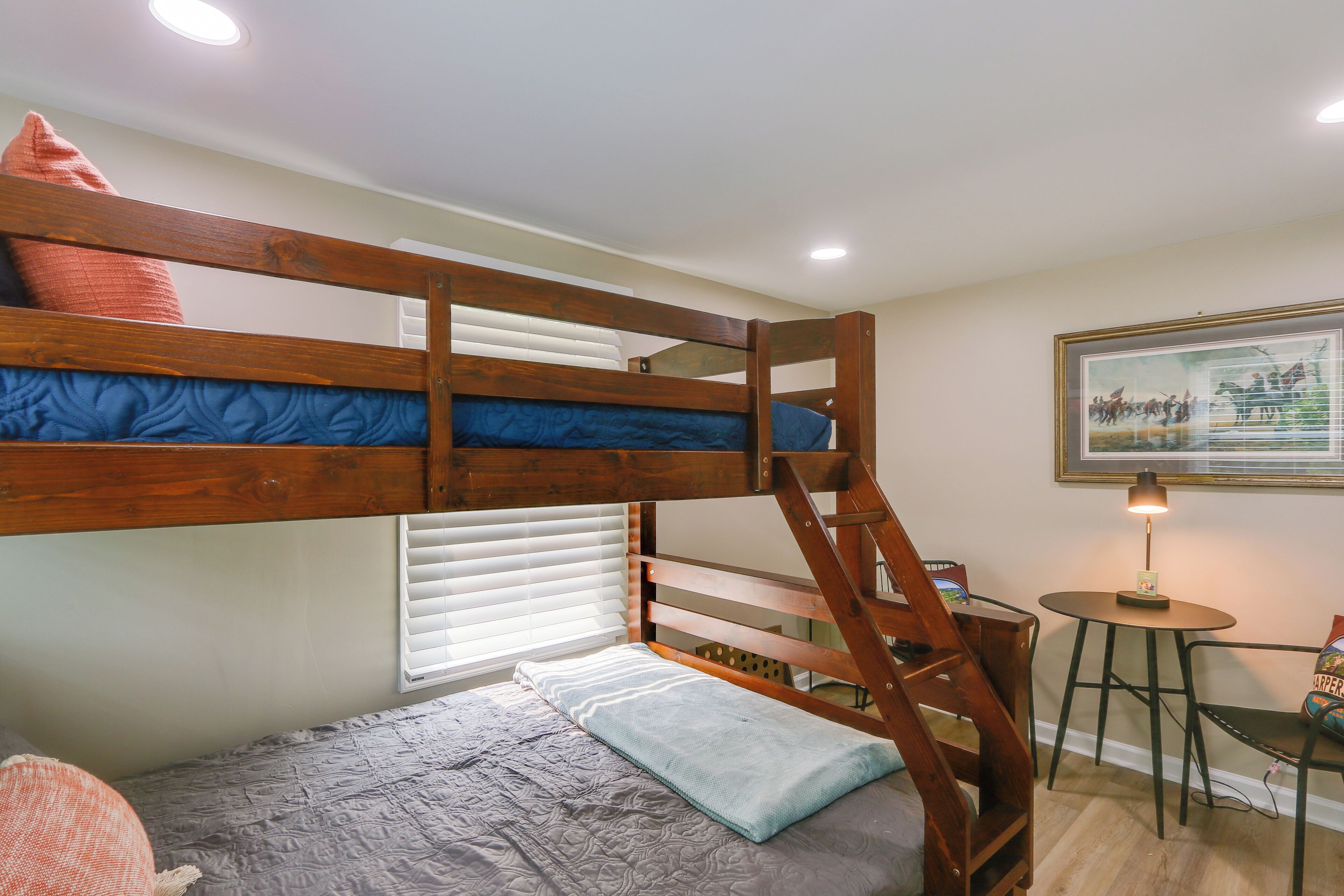 A bunk bed with a ladder, a small table with a lamp, and a framed picture on the wall.