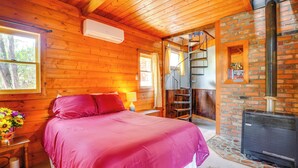 A cozy log cabin bedroom with a large bed, a fireplace, and a wooden staircase. - Bisbee Vacation Rental w/ Mountain Views & Sunroom (Bisbee)