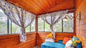 A cozy cabin room with wooden walls, a blue sofa, and a window with curtains. - Bisbee Vacation Rental w/ Mountain Views & Sunroom (Bisbee)