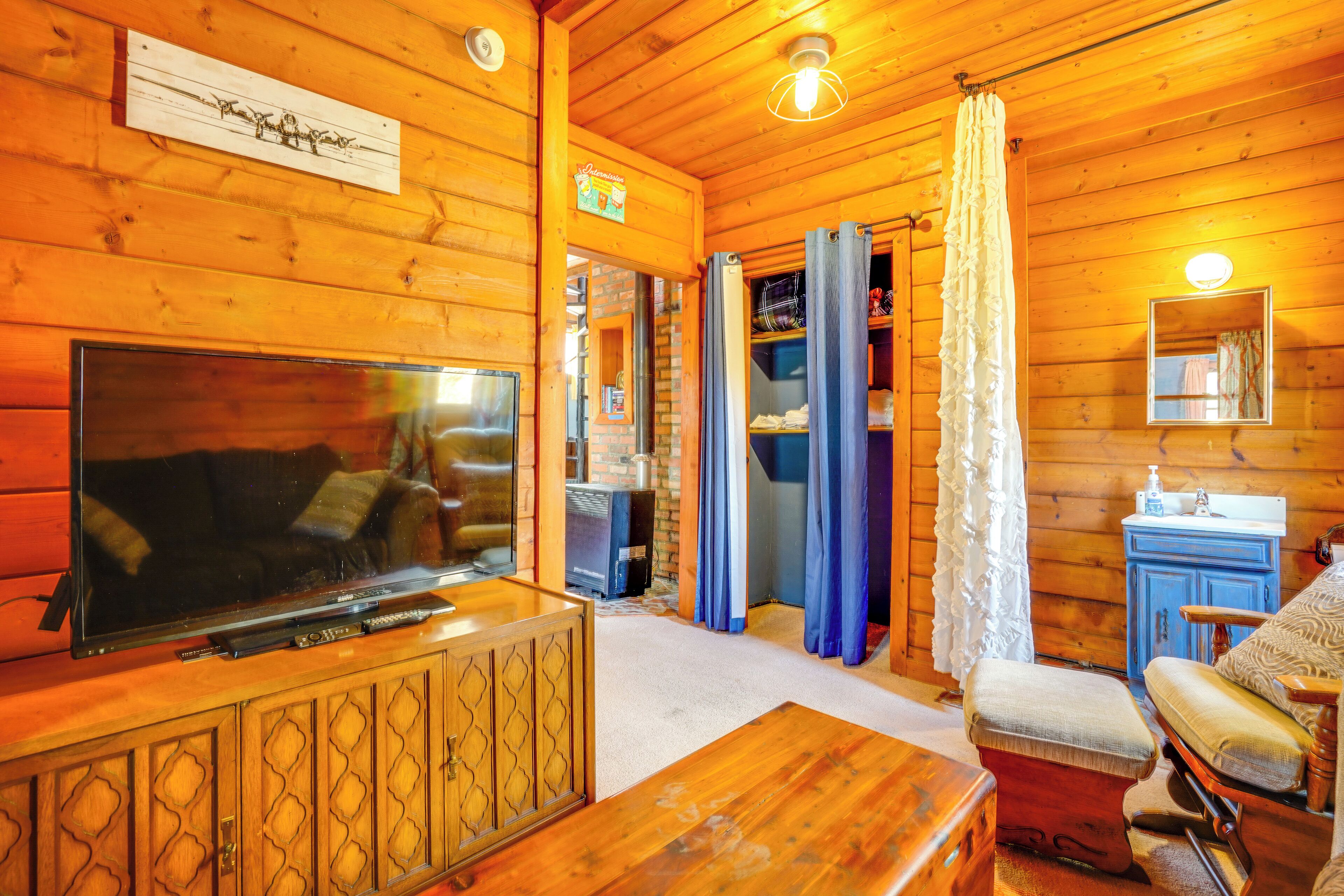 L’intérieur chaleureux d’un chalet, avec un revêtement mural en bois, un téléviseur, un canapé, une table à manger et une salle de bain équipée d’un lavabo et d’un miroir.