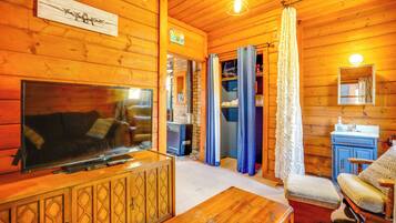 L’intérieur chaleureux d’un chalet, avec un revêtement mural en bois, un téléviseur, un canapé, une table à manger et une salle de bain équipée d’un lavabo et d’un miroir.