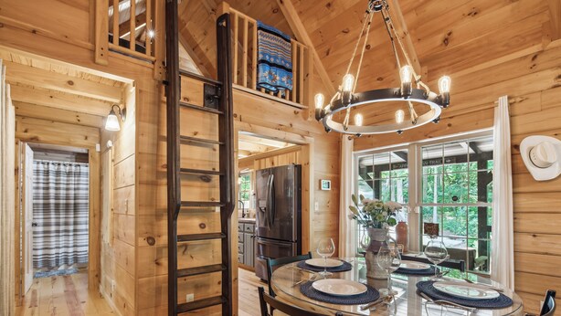 A wooden cabin interior with a dining table set for two, a chandelier, and a view of the outdoors. - Pet-friendly Lake Lure Cabin w/ Outdoor Oasis! (Rutherfordton)