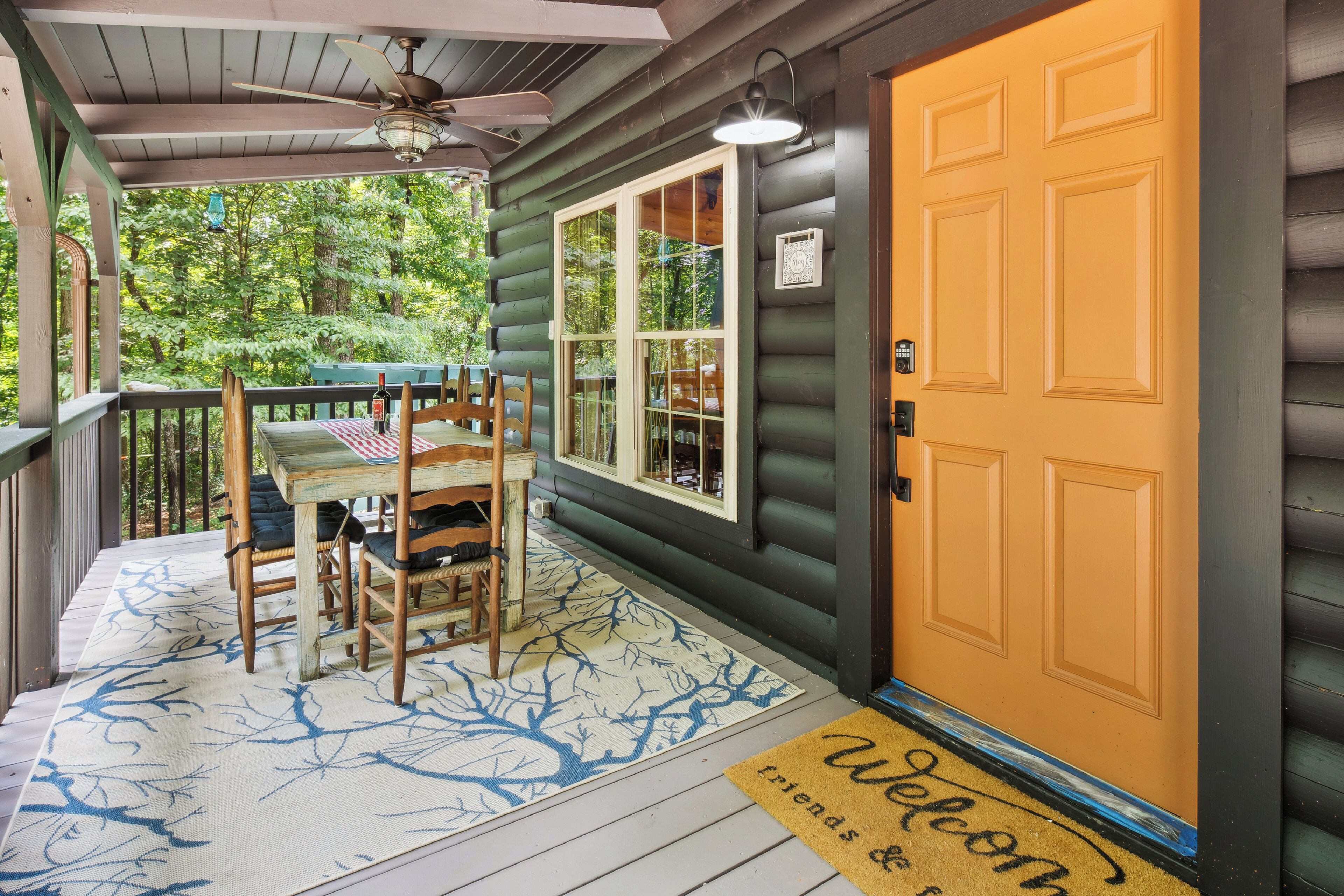 A wooden porch with a table and chairs, a welcome mat, and a door with a window.