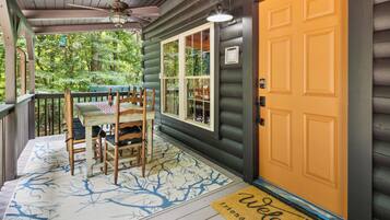 A wooden porch with a table and chairs, a welcome mat, and a door with a window.