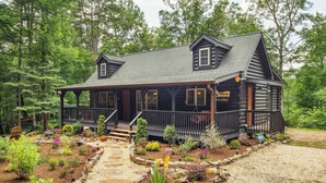 A log cabin with a porch, surrounded by a garden with various plants and a stone pathway leading to the entrance. - Pet-friendly Lake Lure Cabin w/ Outdoor Oasis! (Rutherfordton)