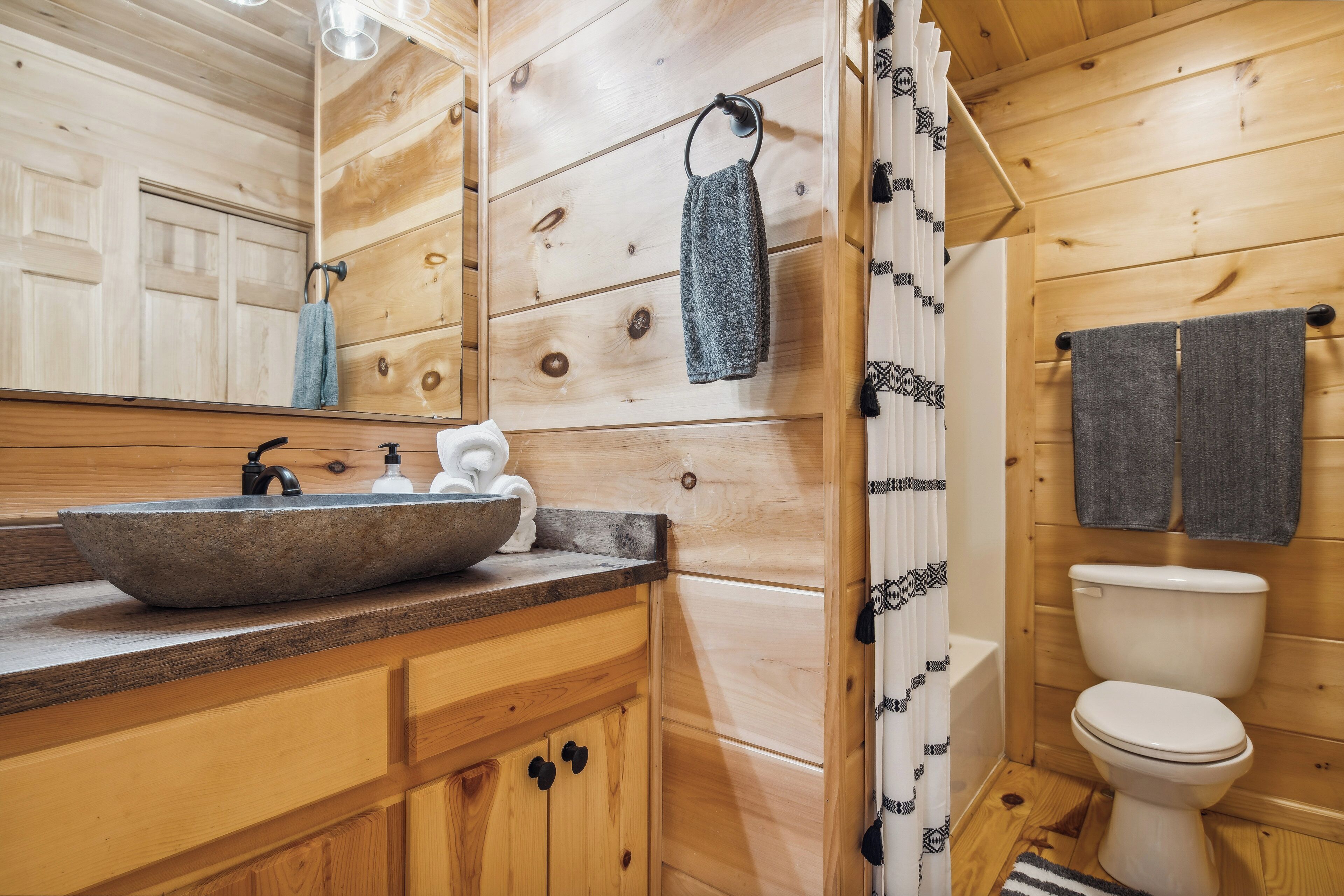 Une salle de bain rustique, aménagée dans une cabane en bois, avec un lavabo en pierre, des toilettes et un rideau de douche.