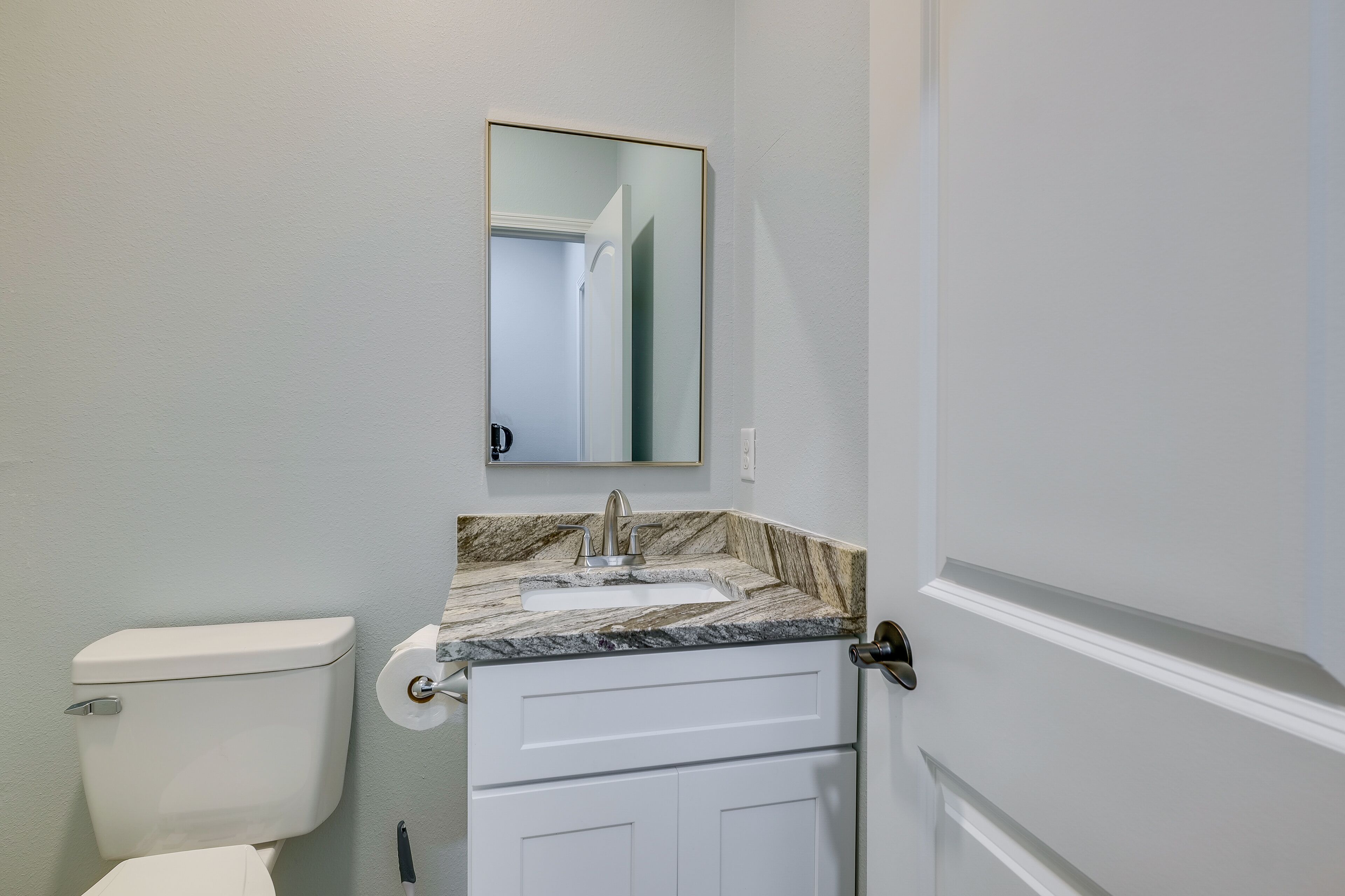 A bathroom with a toilet, sink, and mirror.