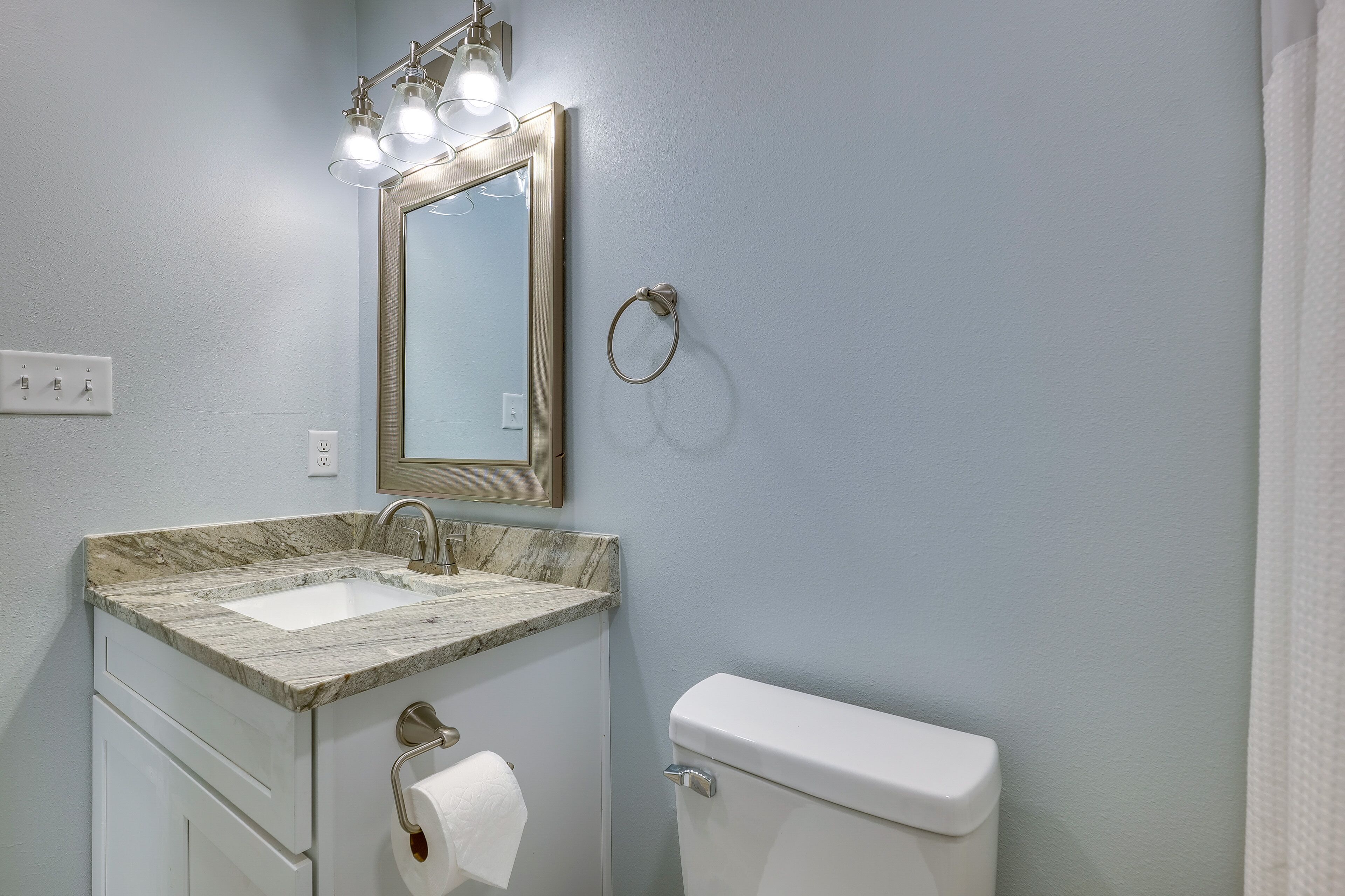 Un baño con lavamanos de mármol, inodoro y espejo con luces.