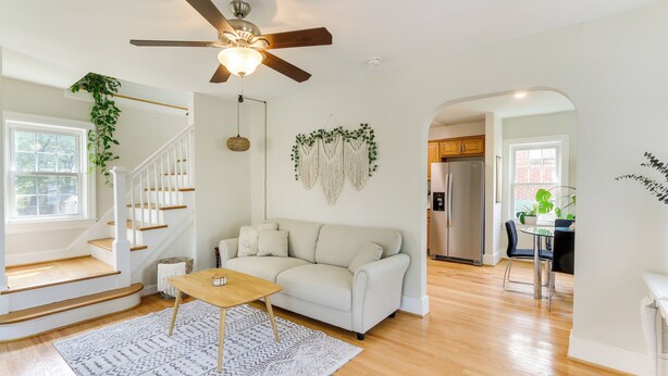 A spacious living room with a white sofa, wooden flooring, a ceiling fan, and a staircase leading to another level. - Chic Front Royal Retreat Near Shenandoah River! (Front Royal)