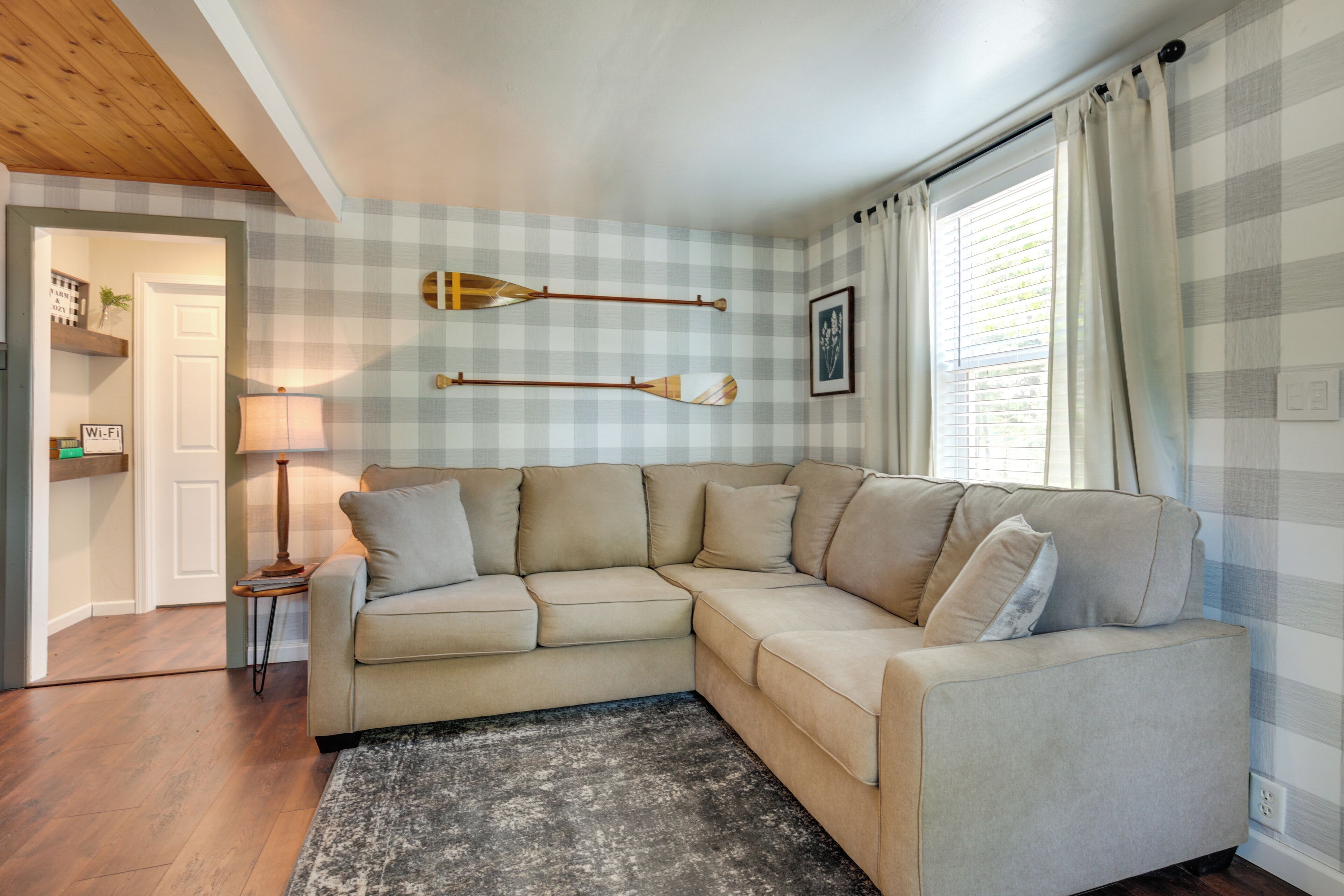 Un salon avec un canapé d’angle beige, une petite table d’appoint, une lampe et un mur à motifs à carreaux.