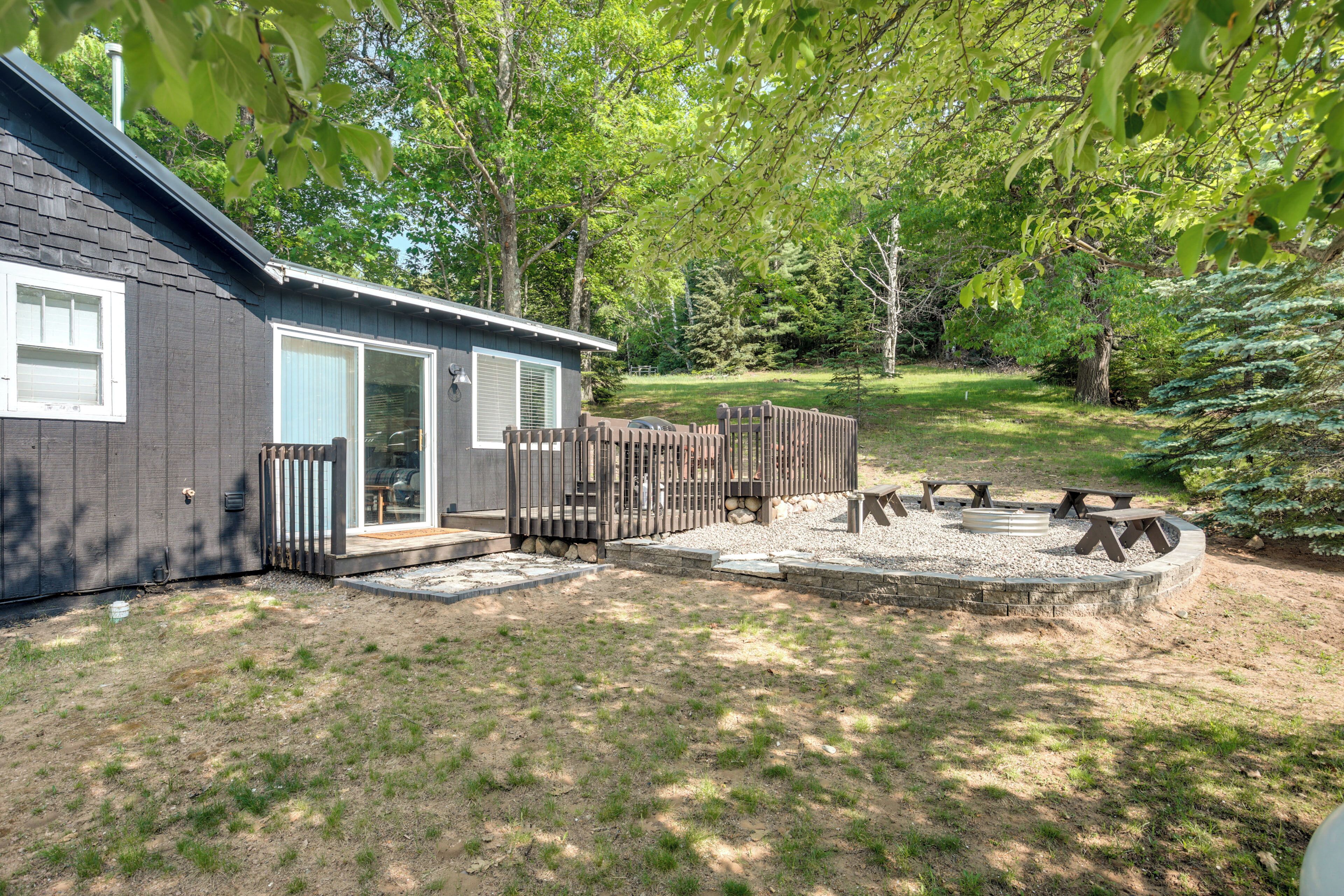 A small cabin with a deck, a fire pit, and a fenced outdoor area.