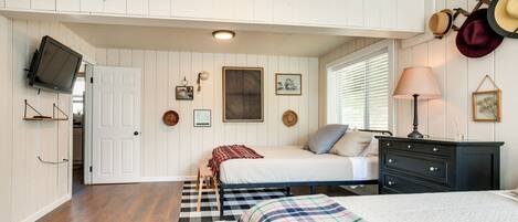 A bedroom with two beds, a TV, a dresser, and a window with blinds.