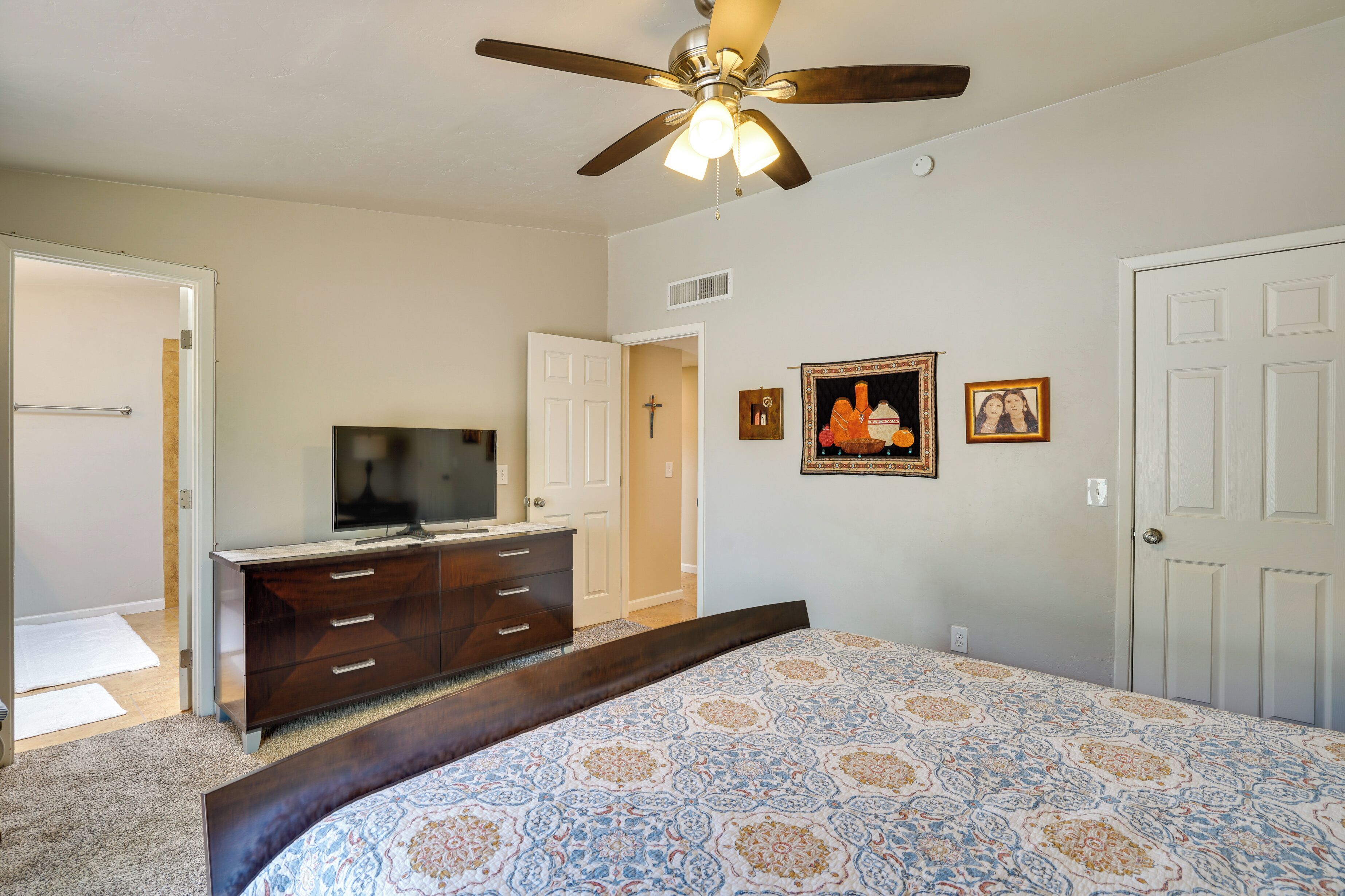 A bedroom with a bed, a dresser, a television, and a ceiling fan.