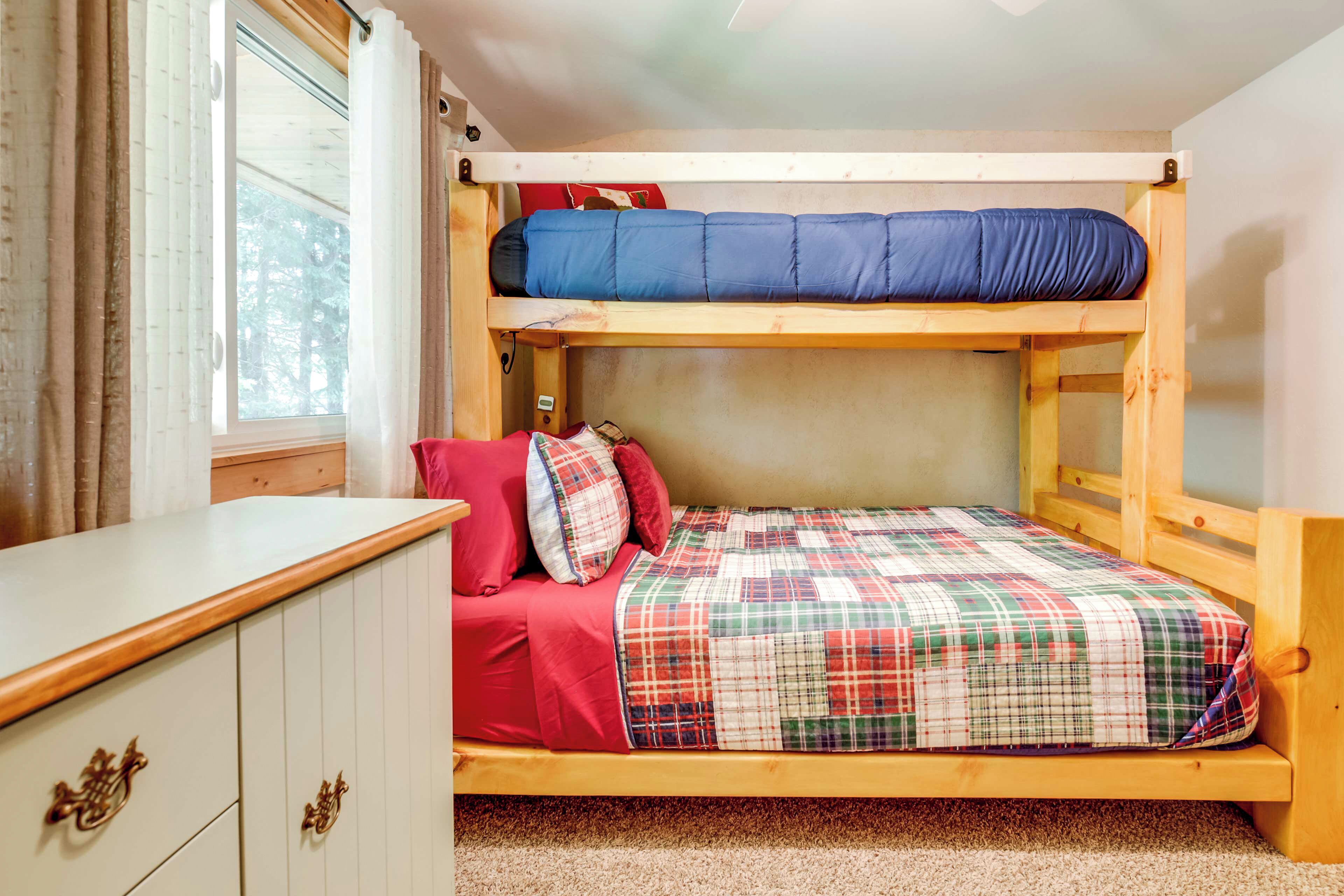 Una cama litera con colchón rojo y azul, una colcha escocesa y un cabecero de madera.
