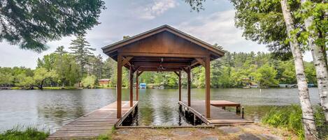 A wooden gazebo with a bench, overlooking a calm lake, surrounded by trees.