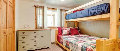 Un dormitorio con una cama doble, un aparador, un ventilador de techo y una ventana con cortinas.