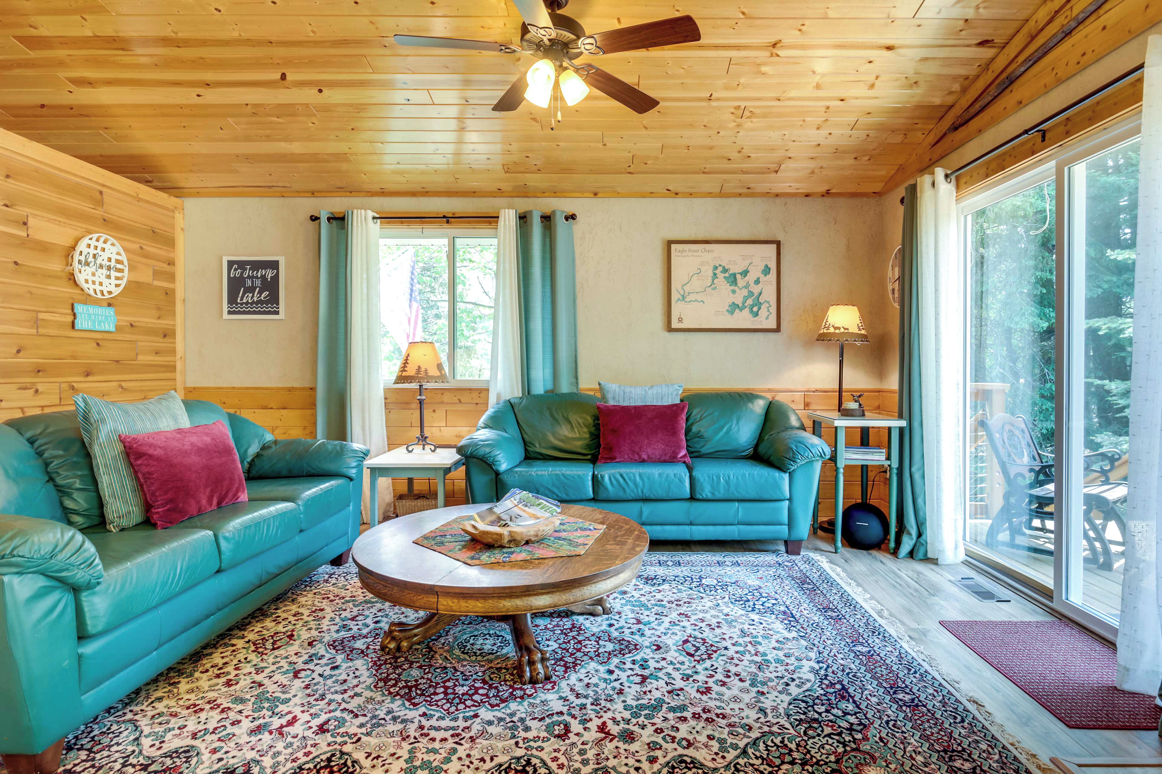 A cozy cabin interior with two teal leather sofas, a wooden coffee table, and a large window offering a view of the outdoors.