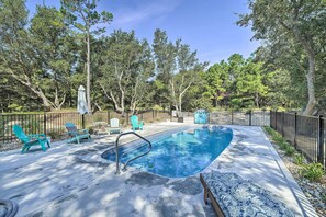 A swimming pool with a metal ladder, surrounded by a black fence. There are two turquoise Adirondack chairs and a covered umbrella. - Kitty Hawk Vacation Rental w/ Pool (Kitty Hawk)