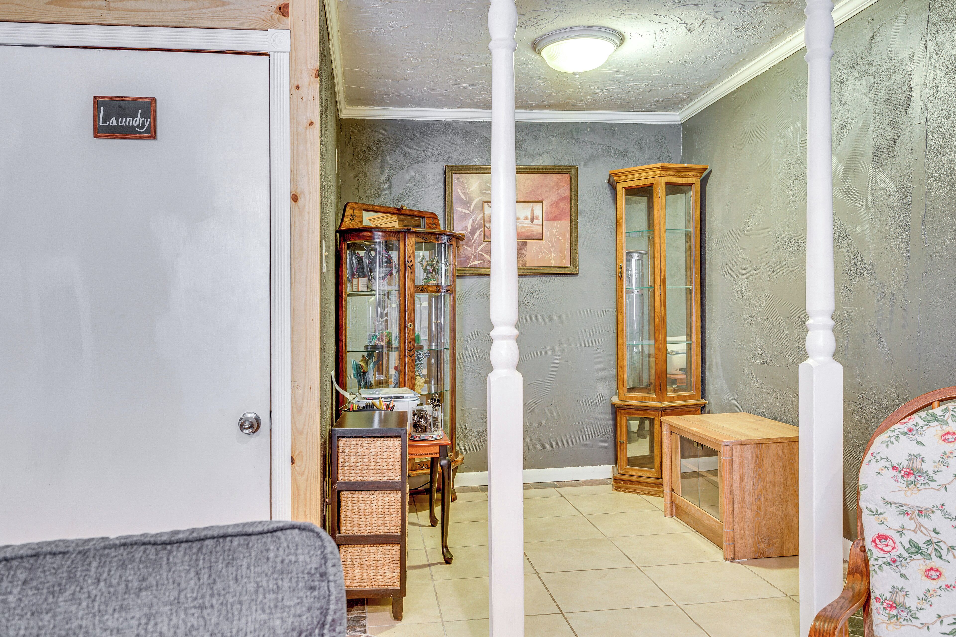 Una habitación con un letrero de lavandería, un armario de madera, una silla de mimbre y una silla estampada con motivos florales.