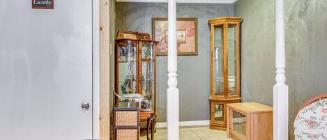 Una habitación con un letrero de lavandería, un armario de madera, una silla de mimbre y una silla estampada con motivos florales.