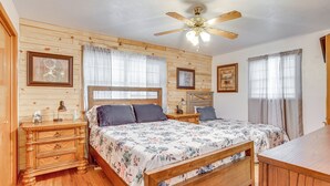 A bedroom with wooden panel walls, a wooden bed with a floral bedspread, two bedside tables with lamps, and a ceiling fan.