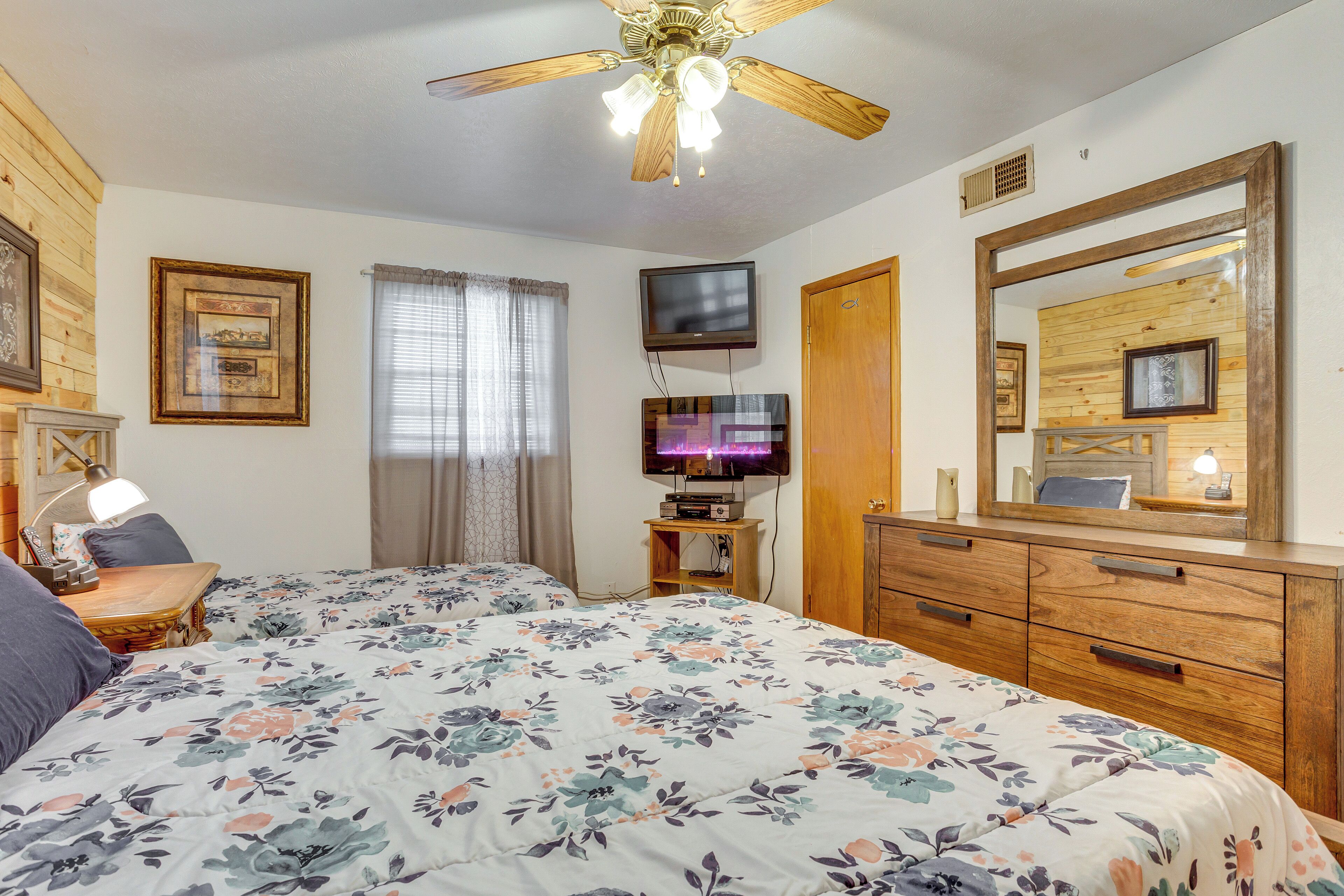 A bedroom with a large bed, a ceiling fan, a TV, wooden furniture, and framed pictures on the walls.