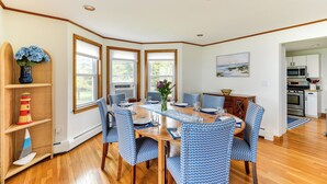 A dining area with a wooden table, blue patterned chairs, and a vase of flowers. - Waterfront Massachusetts Vacation Rental w/ Deck (Westport Point)