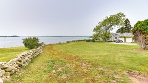 A grassy area with a stone wall, a large tree, and a house with a driveway. - Waterfront Massachusetts Vacation Rental w/ Deck (Westport Point)
