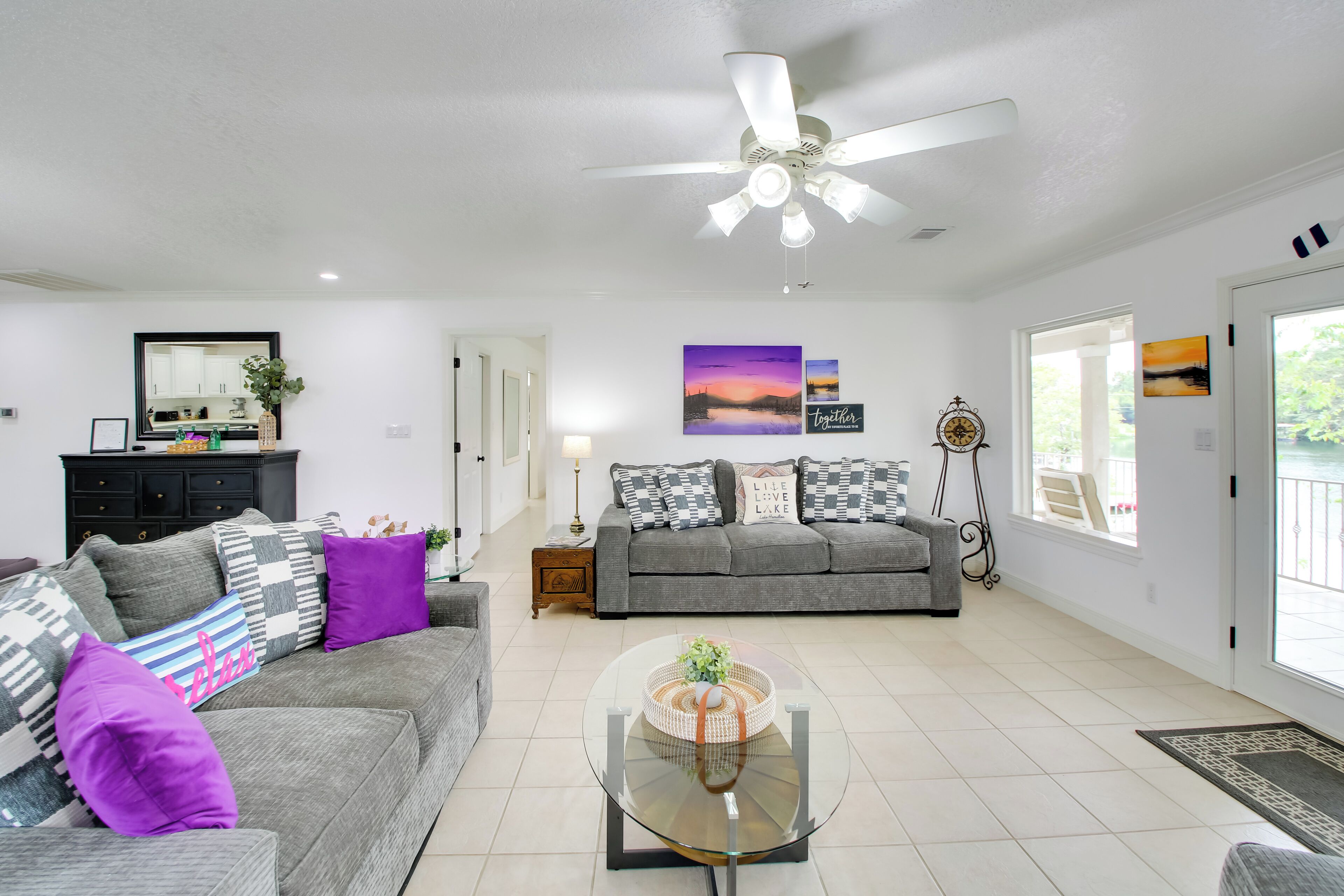 A living room with a grey sofa, a glass coffee table, and a ceiling fan.