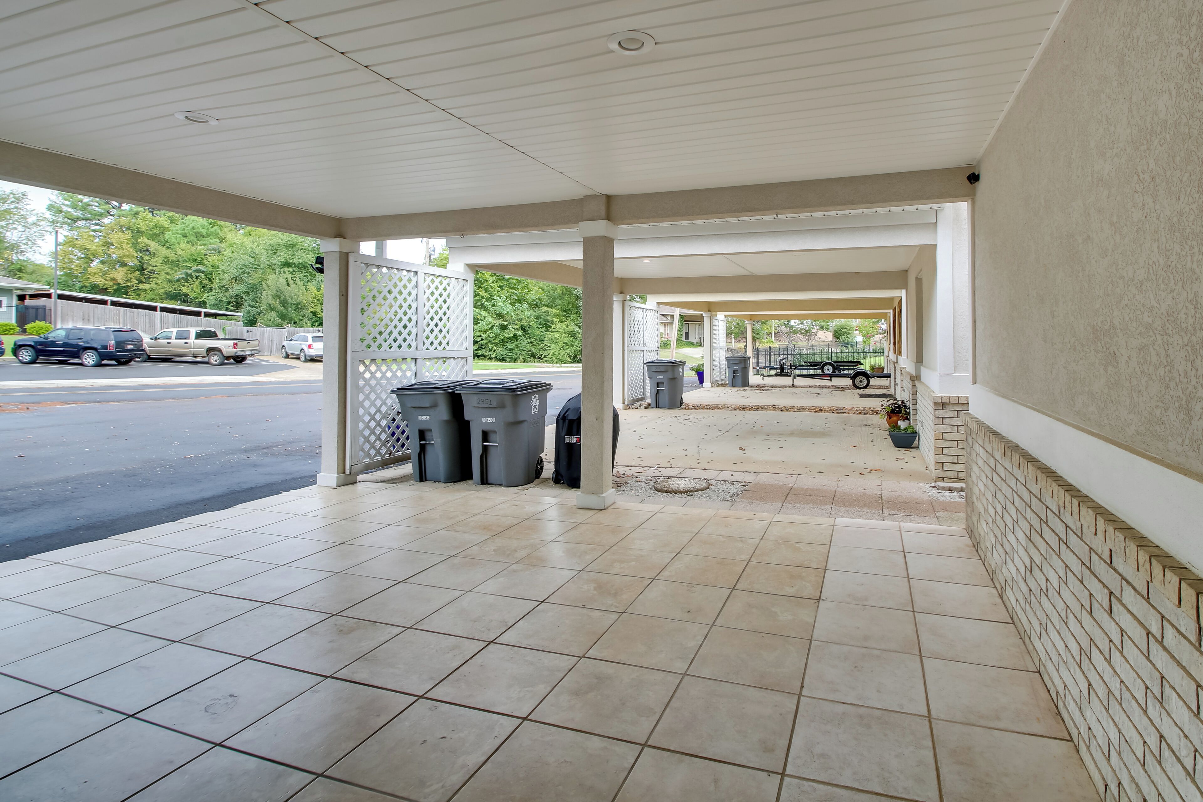 A covered outdoor area with tiled flooring, trash bins, and a brick wall.