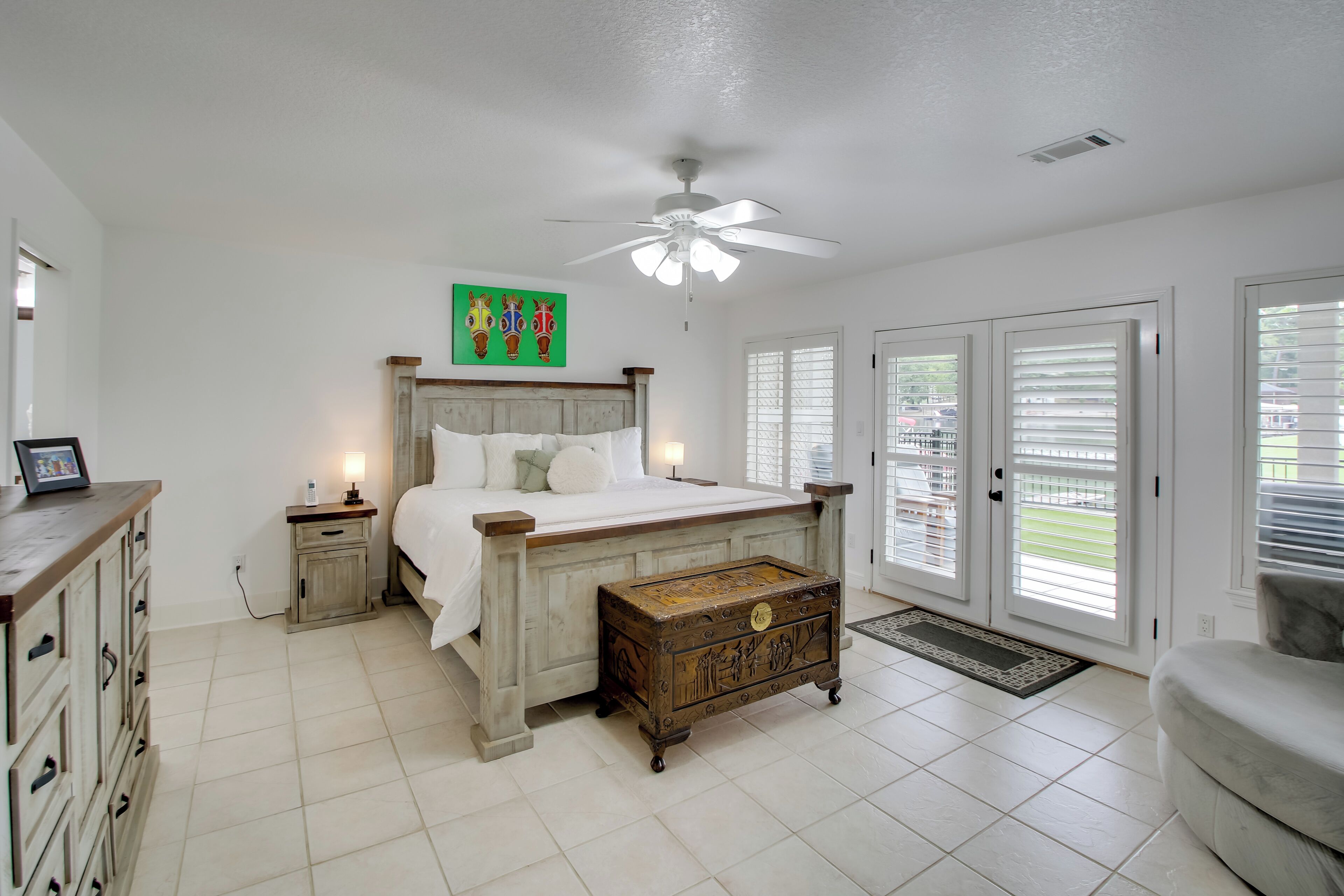 A bedroom with a bed, nightstands, a wooden chest, a ceiling fan, and a view through the door.