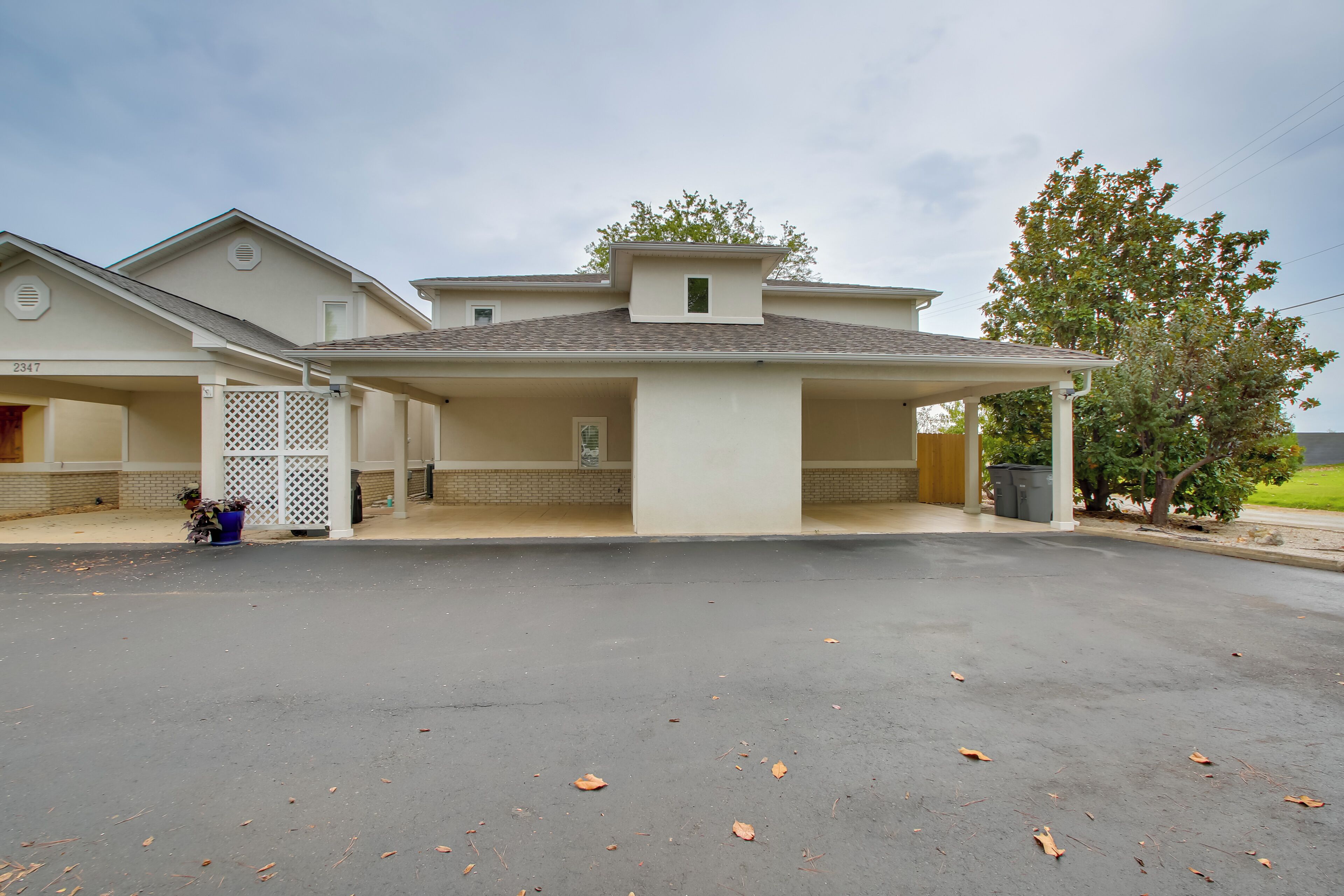 A residential building with a covered garage, a small attached structure, and a tree in front.