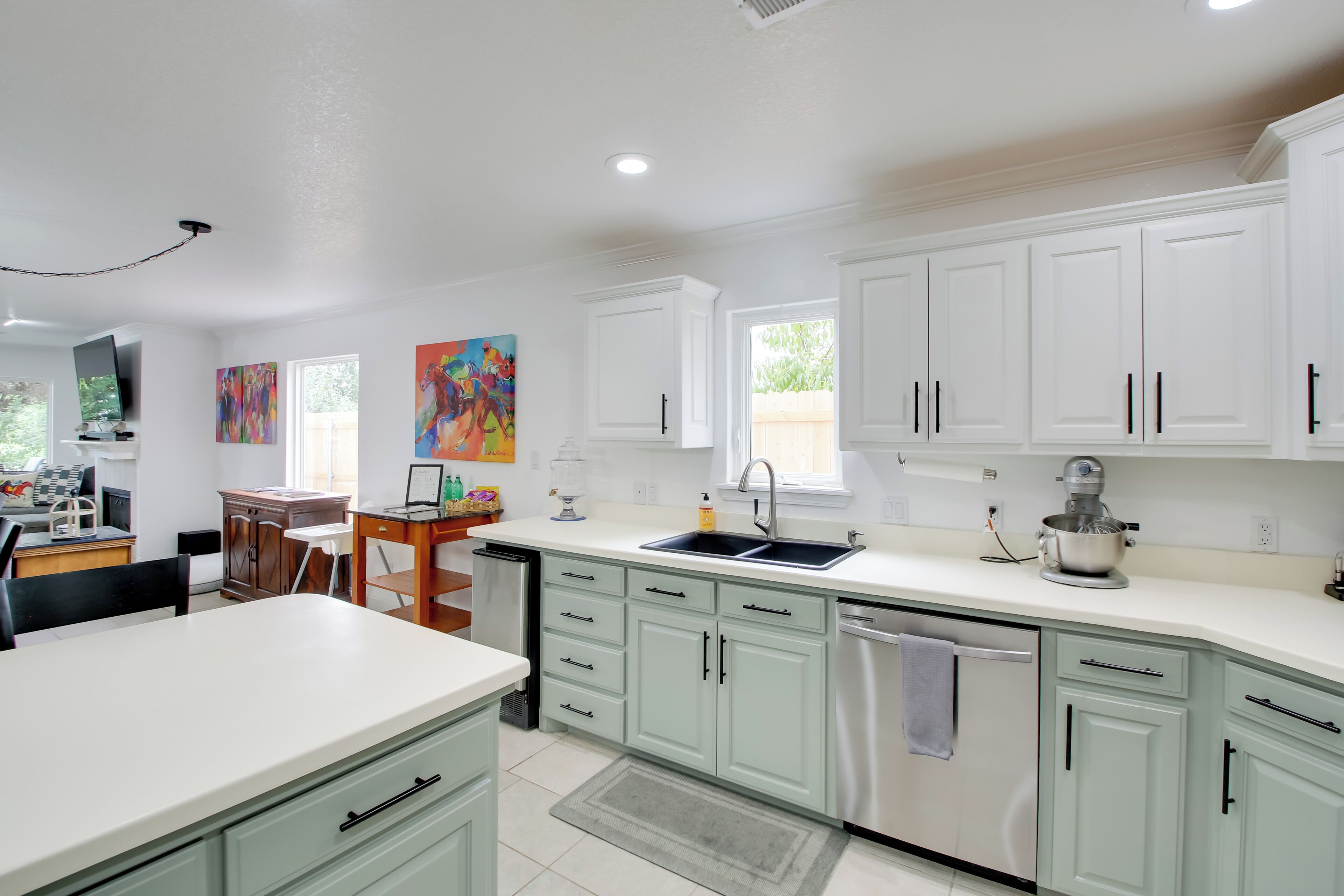A modern kitchen with white cabinets, a stainless steel dishwasher, and a dining area with a table and chairs.