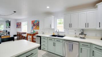 A modern kitchen with white cabinets, a stainless steel dishwasher, and a dining area with a table and chairs.