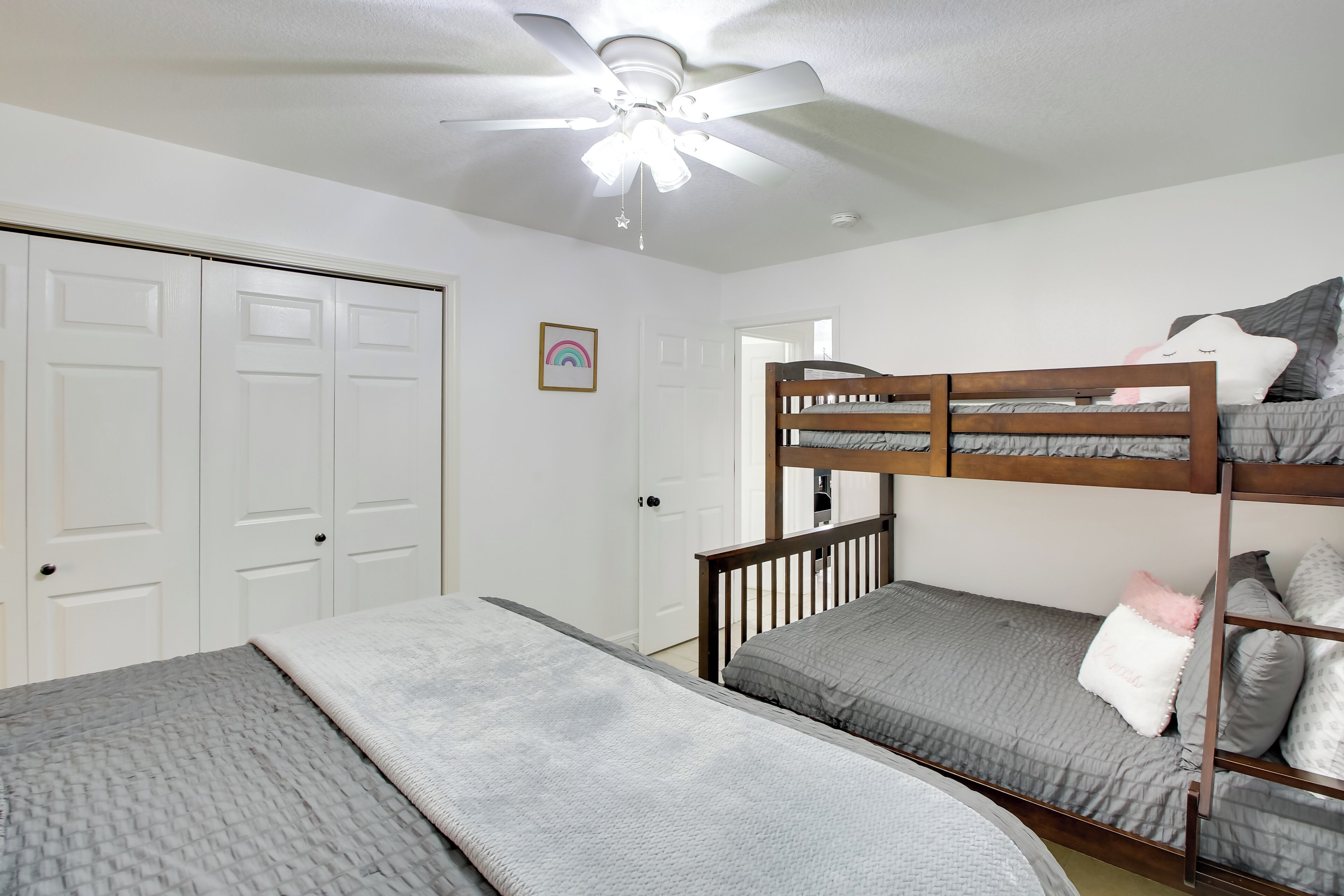 A bedroom with two bunk beds, a ceiling fan, and a door with a rainbow decoration.