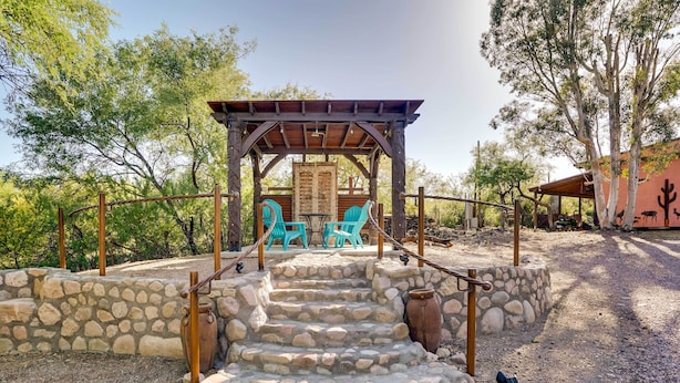 Un escalier en pierre mène à une pergola en bois agrémentée de chaises turquoise.