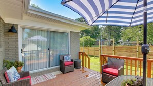 A covered outdoor deck with wicker furniture, a large umbrella, and a sliding glass door leading to a patio.